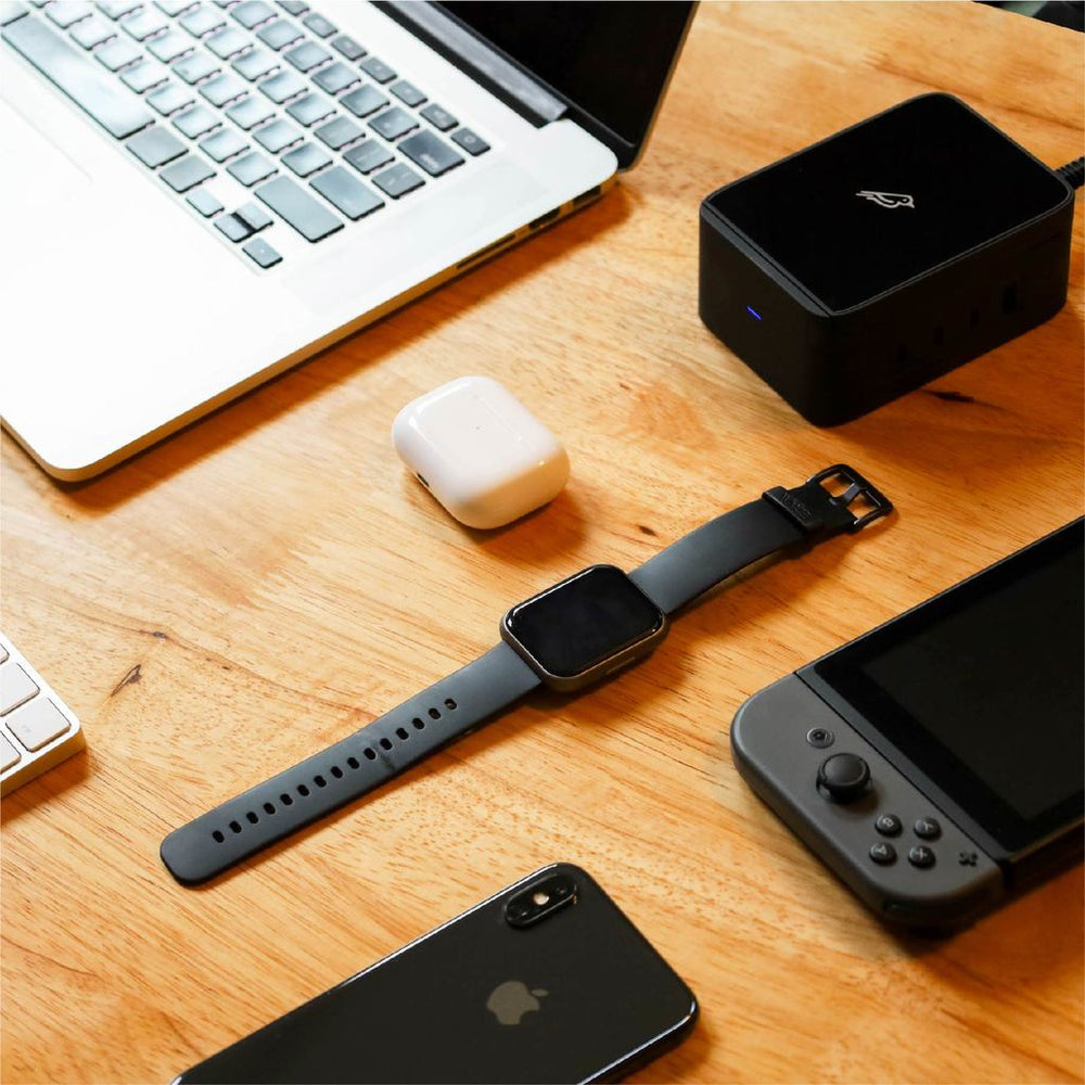 Black Spruce placed next to the five assorted devices it can charge: AirPods Pro, Apple Watch, iPhone, MacBook Pro, and Nintendo Switch