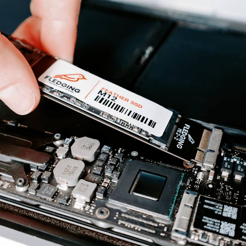 M12 Feather SSD getting pushed into the SSD port of an opened MacBook