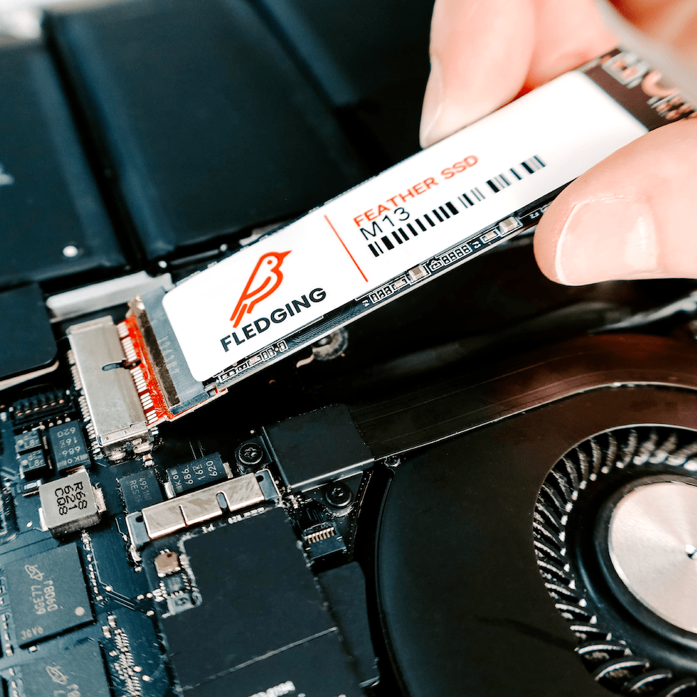 M13-S Feather SSD getting pushed into the SSD port of an opened MacBook