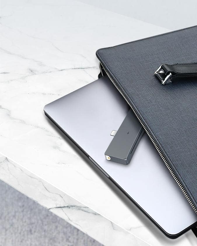 Gray-scale environment: White marble table with an unzipped leather bag, exposing a MacBook and Shell Slim stacked