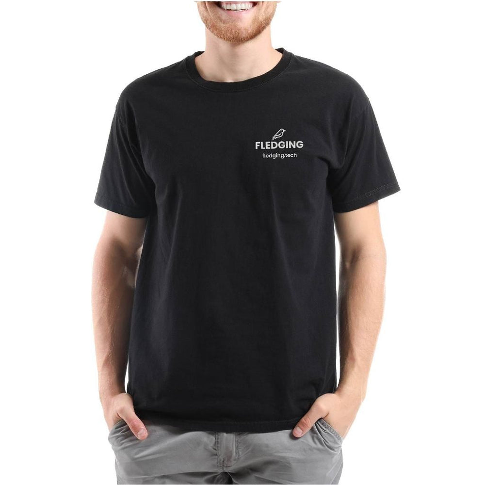 Smiling man wearing black Spruce t-shirt. Hands in pockets of grey pants.