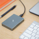 Space Gray rectangular aluminum case with centered Fledging bird logo engraved on the top, plugged into MacBook via Thunderbolt 3 cable.
